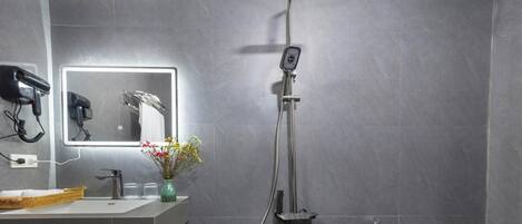 A modern bathroom with a grey tiled wall, a sink with a mirror, a handheld showerhead, and a toilet.