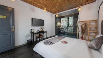 Habitación de hotel moderna con una cama grande, un escritorio con silla, televisión y ventana con vista a árboles.