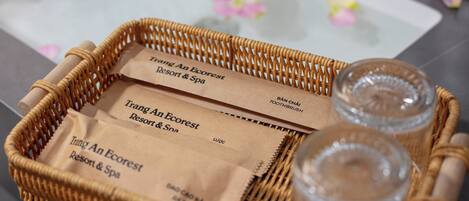 A wicker tray with two glass jars and two brown paper bags labeled "Trang An Ecorest Resort & Spa".
