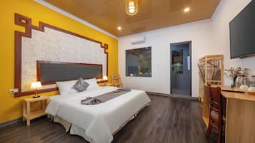 Hotelkamer met een groot bed, nachtkastjes, een bureau met stoel, een flatscreen televisie en een groot raam.