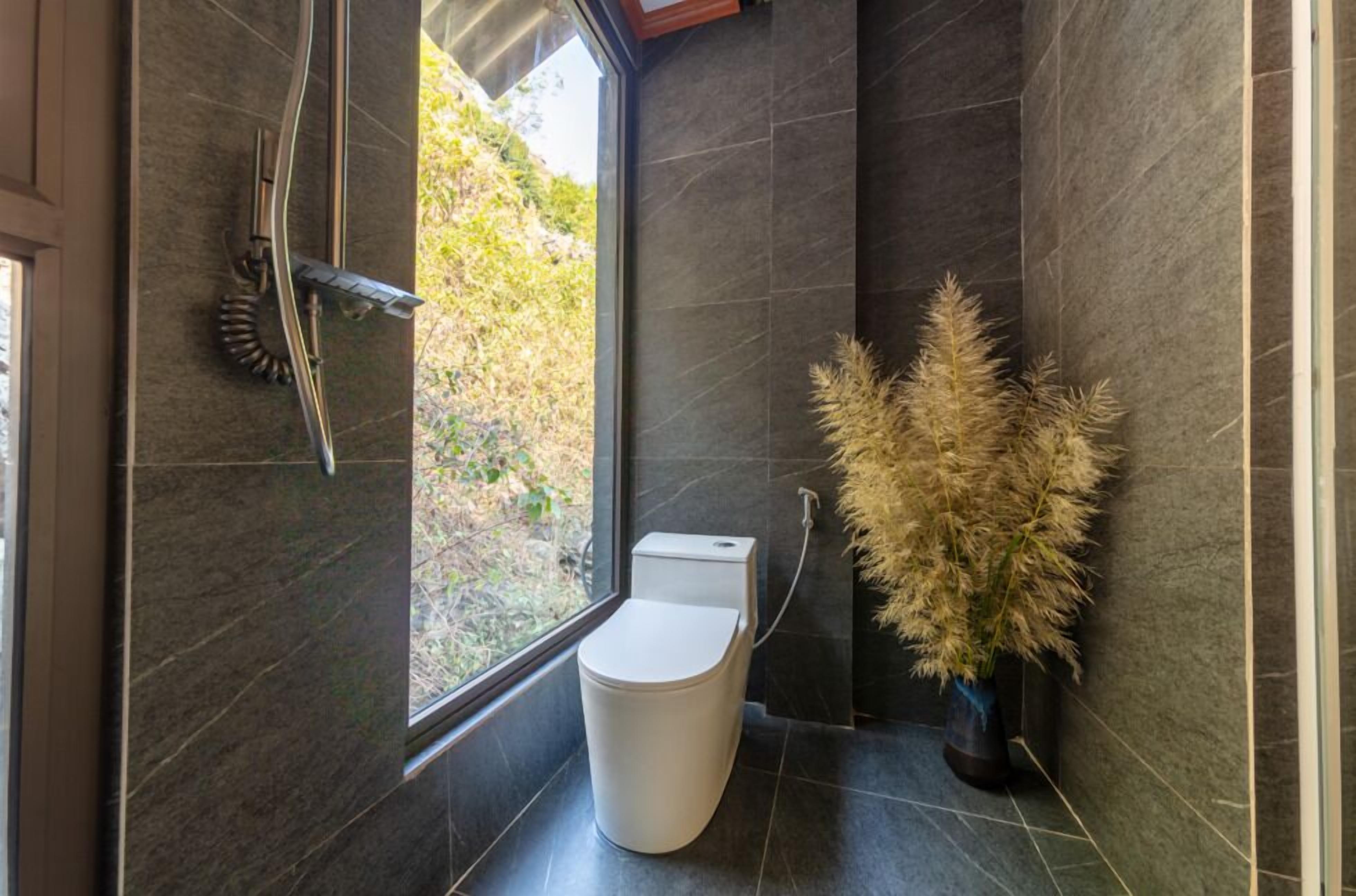 A modern bathroom with a toilet, a shower, and a large window.