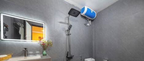 A modern bathroom with a large mirror, a showerhead, a toilet, and a sink with a vase of flowers.