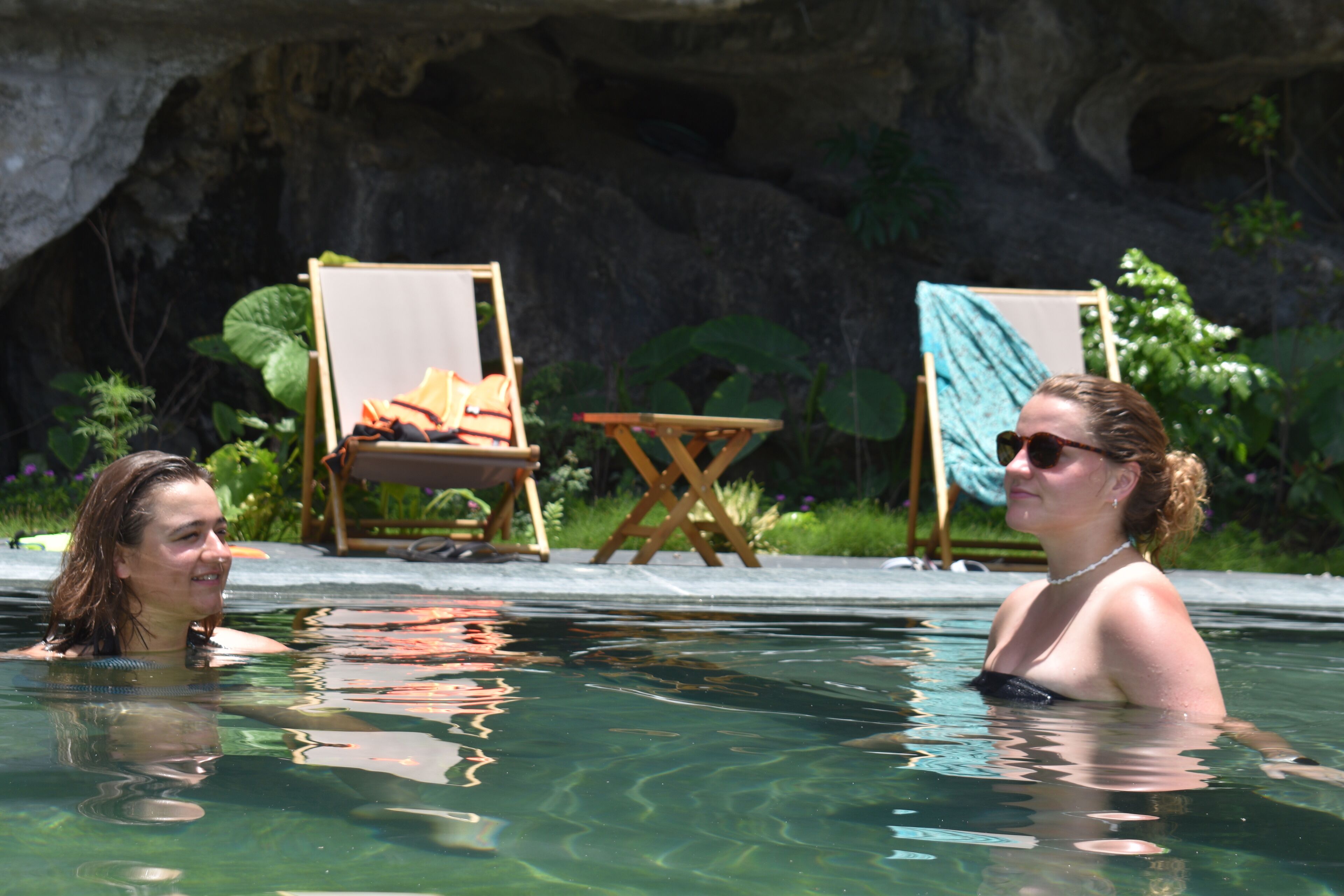 Dos personas en una piscina con sillas y un cuadro al fondo.
