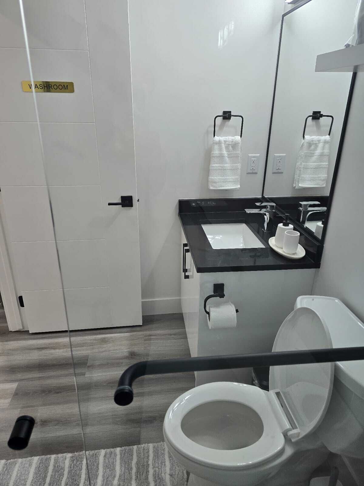 A modern bathroom with a toilet, sink, and mirror. There is a handrail for accessibility.