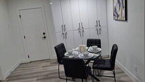Zona pranzo con tavolo rotondo apparecchiato per quattro, circondato da sedie nere. Sullo sfondo, mobili contenitori bianchi con maniglie nere.