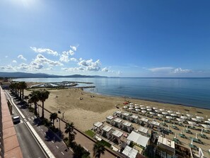 A beach with umbrellas and lounge chairs, a road parallel to the beach, and a clear sky. - Orizzonte Apartment in Follonica (Follonica)