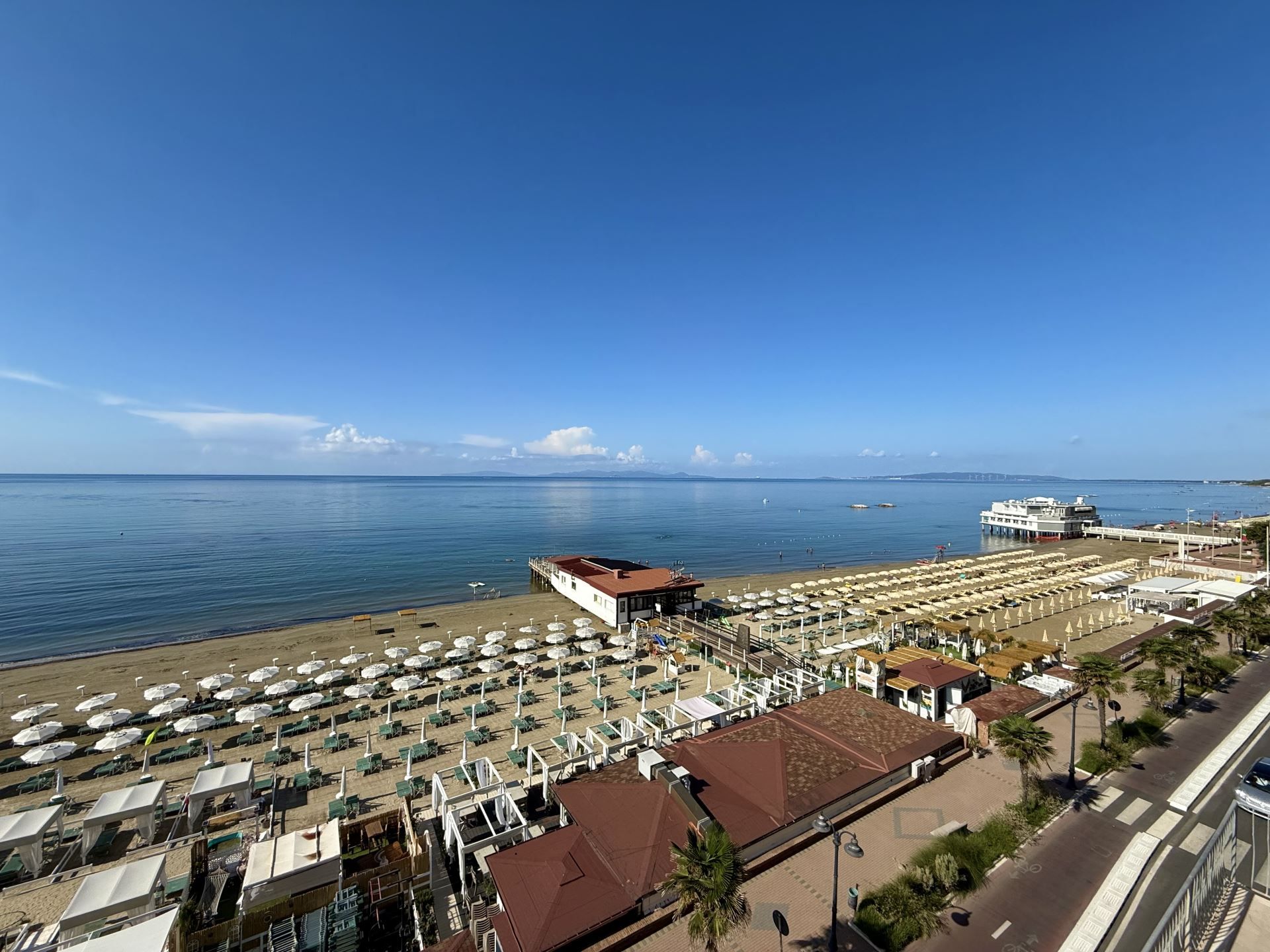 A beachside hotel with multiple sun loungers and umbrellas, a pier extending into the sea, and a clear blue sky. - Orizzonte Apartment in Follonica (Follonica)