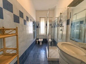 A bathroom with a shower, toilet, bidet, and a sink with a mirror.