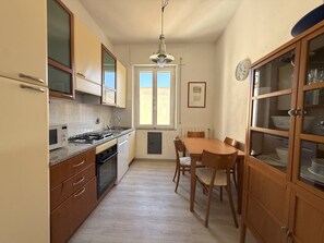 A kitchen with a dining table and chairs, wooden cabinets, a stove, and a window. - Orizzonte Apartment in Follonica (Follonica)