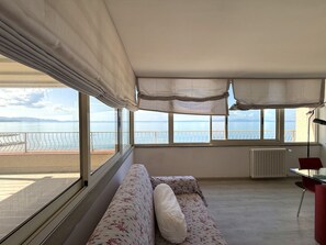 A room with a sofa, a table, and a view of the sea. - Orizzonte Apartment in Follonica (Follonica)