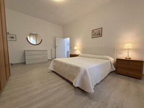 A bedroom with a bed, a dresser, a bedside lamp, a mirror, and a picture on the wall. - Orizzonte Apartment in Follonica (Follonica)