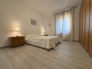 A bedroom with a bed, two bedside tables with lamps, a wooden wardrobe, and a window with curtains. - Orizzonte Apartment in Follonica (Follonica)