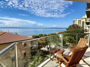 A balcony with wooden chairs and a table, overlooking a coastal view with buildings in the background. - Sunny Apartment in Follonica (Follonica)