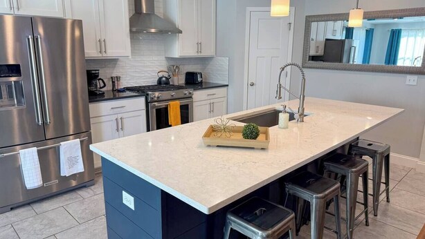A modern kitchen with a large island, stainless steel appliances, and bar stools. - Your Perfect Home Away From Home · Owasso, OK (Owasso)