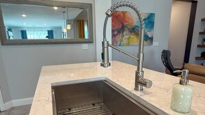 A modern kitchen with a stainless steel sink, a large mirror, and a colorful abstract painting on the wall. - Your Perfect Home Away From Home · Owasso, OK (Owasso)