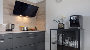 Moderni keittiö, jossa on taulutelevisio, kahvinkeitin ja lasikaapisto viinilaseille.