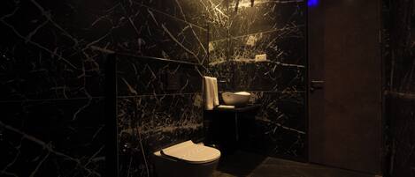 A modern bathroom with a marble wall, a toilet, a sink, and a shower area.