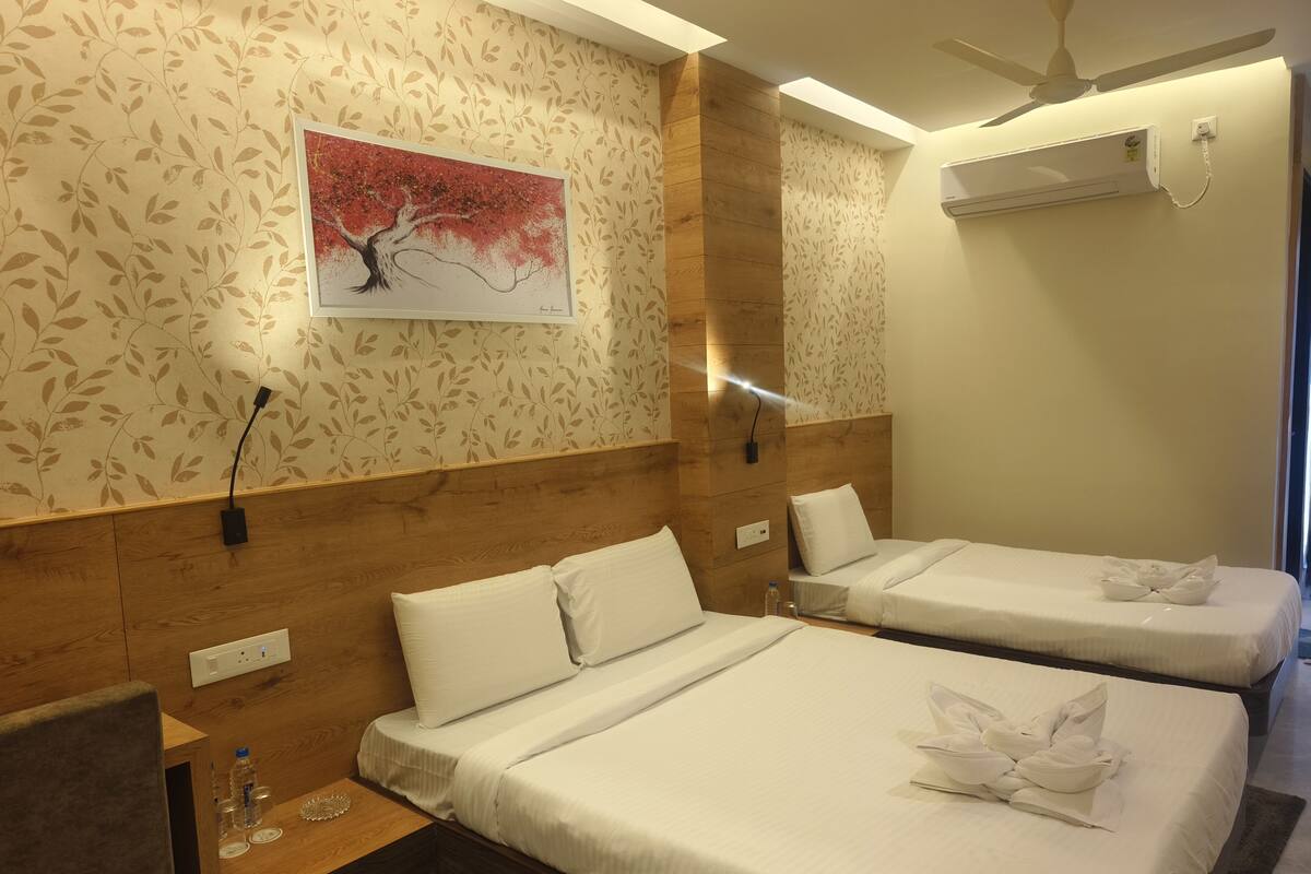 Habitación de hotel con dos camas, cabecero de madera, aire acondicionado de pared y ventilador de techo, además de una obra de arte enmarcada.