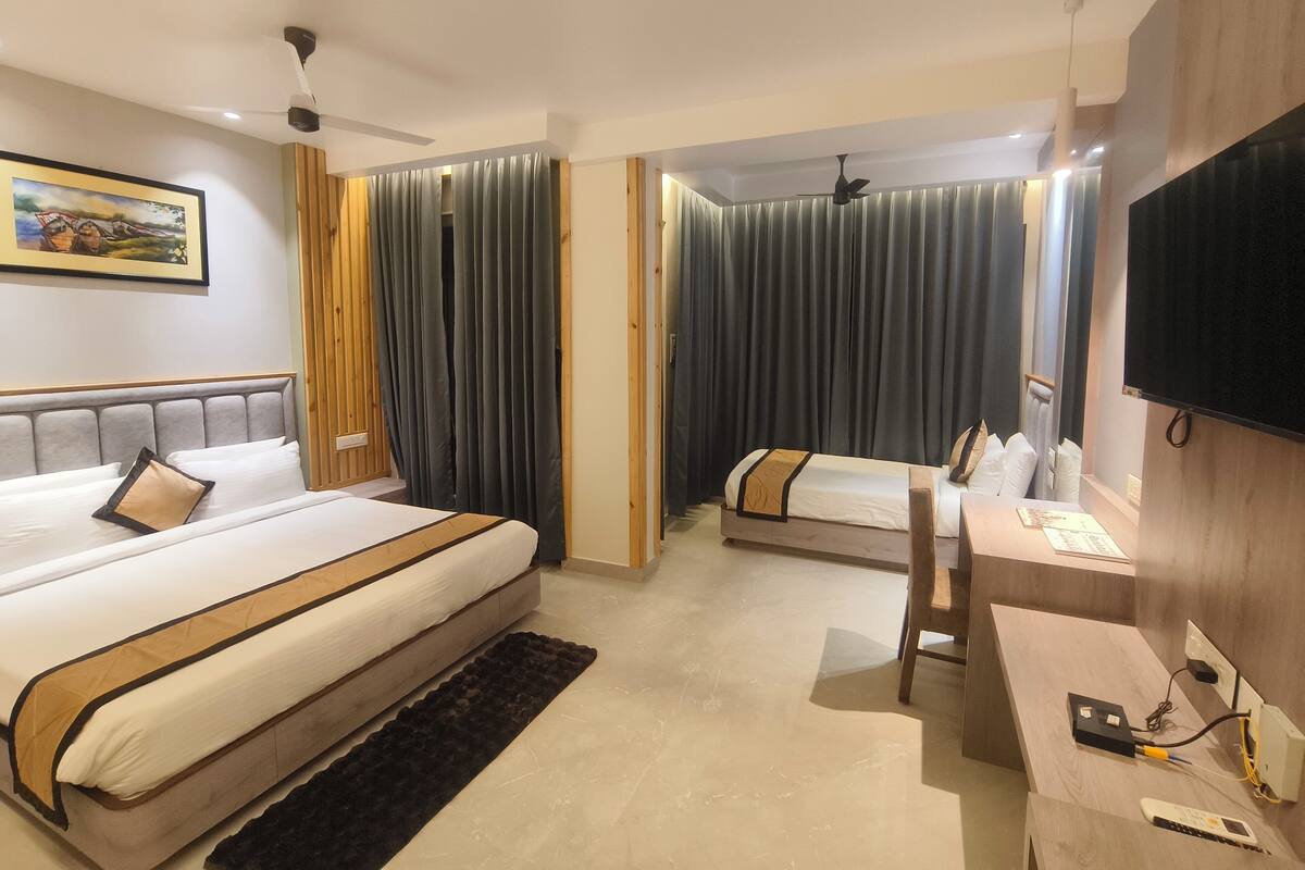 Habitación de hotel con dos camas, un escritorio, un televisor y un ventilador de techo.