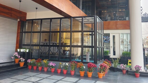 A hotel lobby with a modern design, featuring a glass facade, wooden beams, and potted plants. - Hotel Palace View (Lalbag)