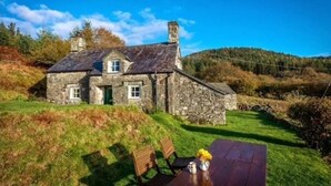 A stone house with a grassy yard and a wooden table with chairs. - Secluded Mountain Stay - Stunning Views of Eryri (Dolgellau)