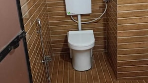 A small, enclosed bathroom with a toilet, a shower, and a wall-mounted heater. - Kokan Inn (Dapoli)
