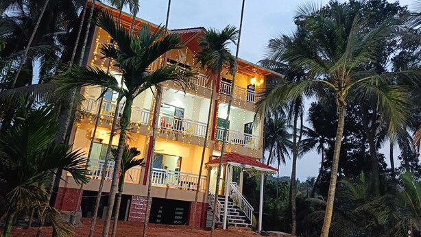 A multi-story building with balconies, surrounded by palm trees. - Kokan Inn (Dapoli)