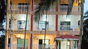 A multi-story building with balconies, a covered entrance, and a dirt ground. - Kokan Inn (Dapoli)