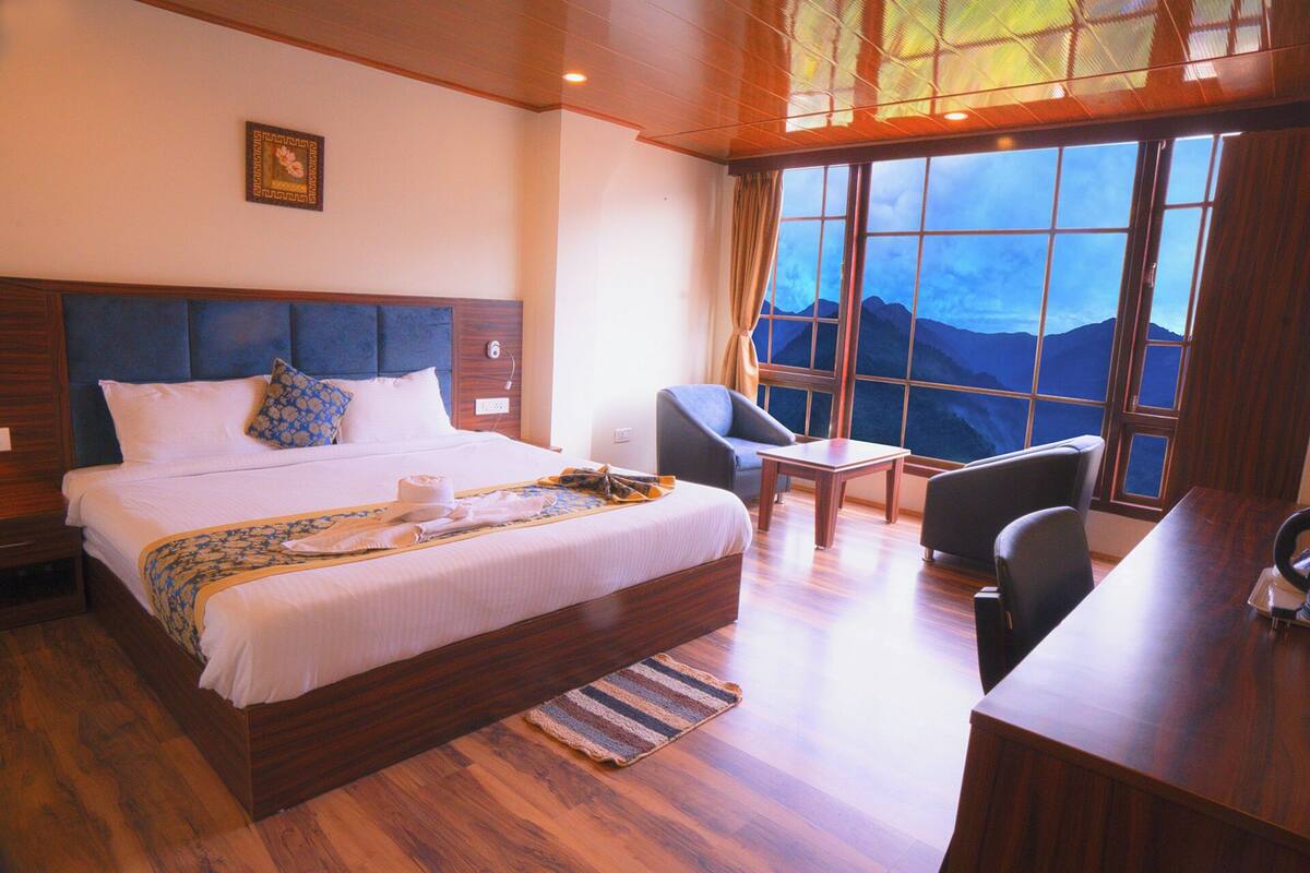 Habitación de hotel con una cama grande, un escritorio, dos sillas y vistas a la montaña desde la ventana.