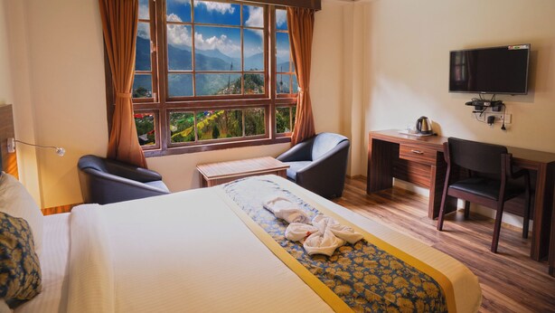 Habitación de hotel con cama, escritorio, silla, televisión y ventana con cortinas.