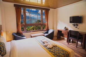 Habitación de hotel con cama, escritorio, silla, televisión y ventana con cortinas.