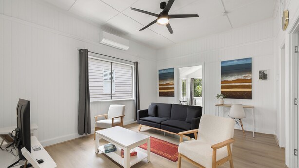A modern living room with a black sofa, white armchairs, a white coffee table, and a ceiling fan. - Wellington House (Mackay)