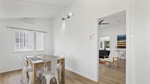A dining area with a wooden table and white chairs, a window with a view, and a door leading to another room. - Wellington House (Mackay)