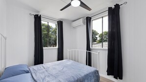 A bedroom with a bed, a ceiling fan, and black curtains on windows. - Wellington House (Mackay)