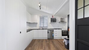 A modern kitchen with white cabinets, a stainless steel dishwasher, an oven, and a microwave. - Wellington House (Mackay)