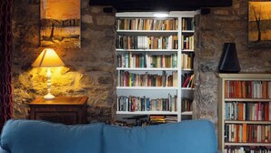 A cozy room with a stone wall, a bookshelf filled with books, a blue sofa, and a lamp. - Large Country House | Games Room & Log Burner (Haverfordwest)