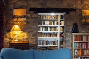 A cozy room with a stone wall, a bookshelf filled with books, a blue sofa, and a lamp. - Large Country House | Games Room & Log Burner (Haverfordwest)
