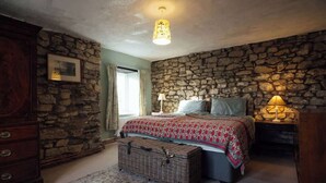 Ein Schlafzimmer mit einer Steinsäule, einem Bett mit gemustertem Überwurf, einem Schminktisch, einer Lampe und einer Korboehle.