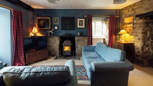 Ein gemütliches Wohnzimmer mit Kamin aus Stein, einem blauen Sofa und einem Fernseher auf einem Holzkabinett.