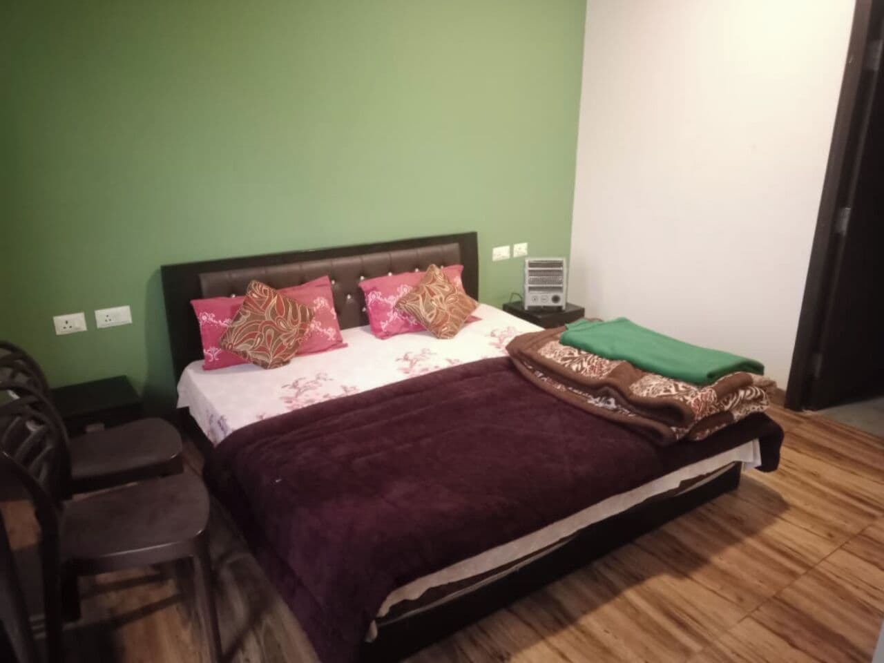 Un dormitorio con cama, paredes verdes, suelo de madera y una mesita de noche.