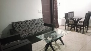 Una sala de estar con un sofá estampado, una mesa de centro de vidrio y una zona de comedor con sillas y una mesa.