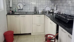 Una cocina pequeña con armarios blancos, una estufa a gas, un lavamanos y un cilindro de gas rojo.
