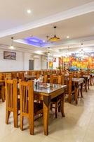 Un vaste espace dédié à la salle à manger, avec de nombreuses tables et chaises en bois, des ventilateurs de plafond et une fresque colorée sur le mur.