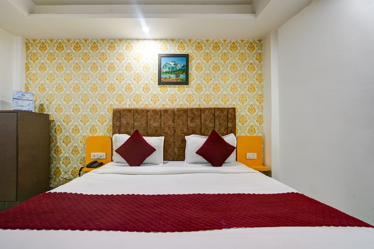 Una habitació d'hotel amb paper tapet motius, un capçal de llit de fusta, un llit amb roba de llit blanca i detalls vermells, i dues taules de nit amb làmpades.