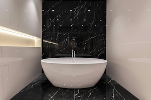 A modern bathroom with a freestanding bathtub, marble walls, and a sleek, illuminated countertop.