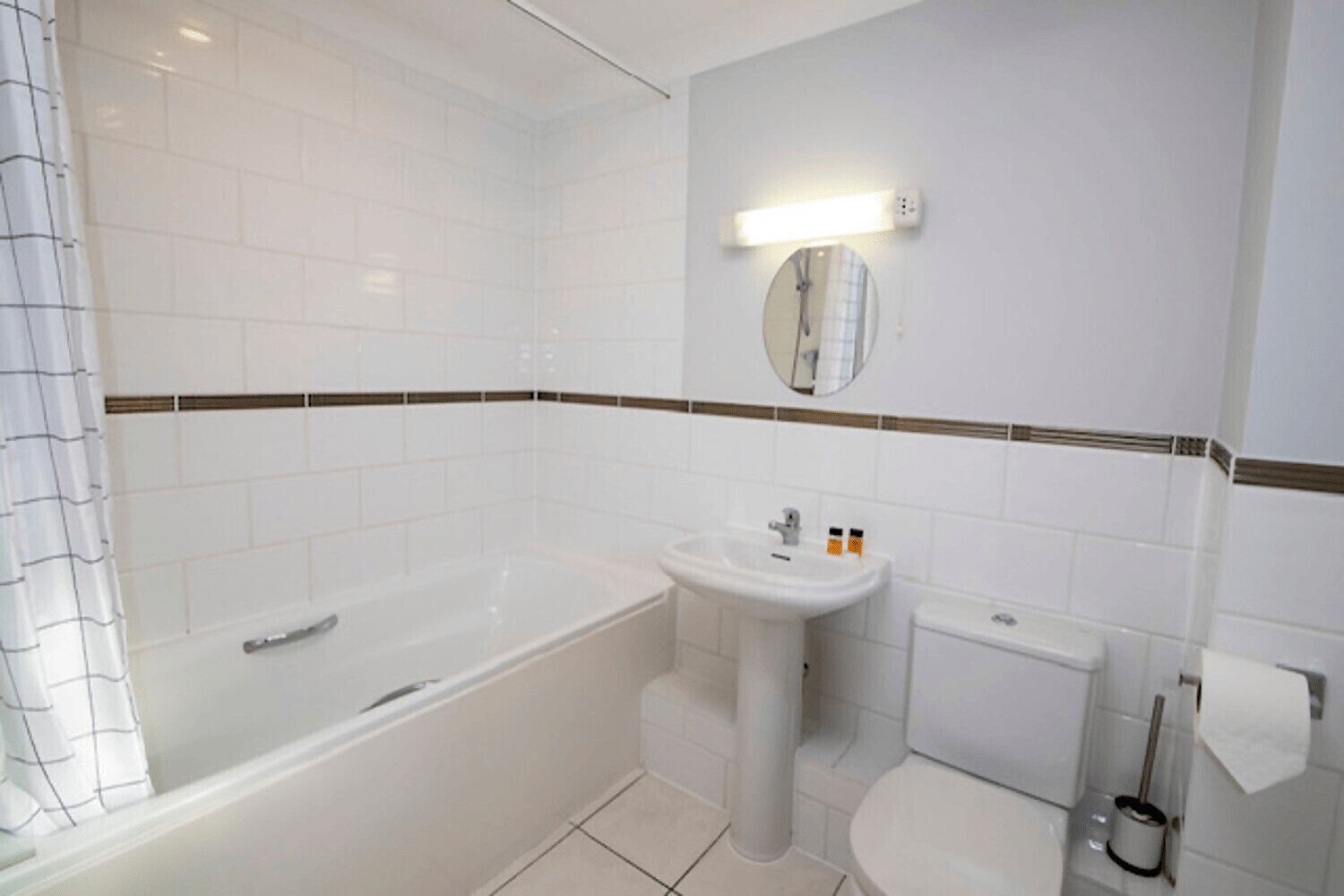 A bathroom with a bathtub, sink, toilet, and a mirror with a light above it.