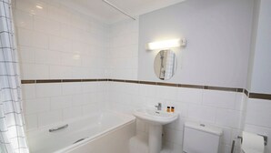 Un baño con bañera, lavamanos, inodoro y espejo con luz superior.