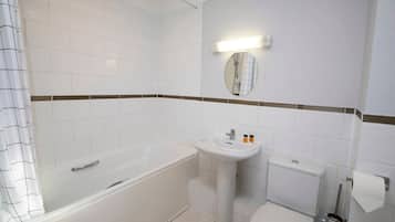 A bathroom with a bathtub, sink, toilet, and a mirror with a light above it.