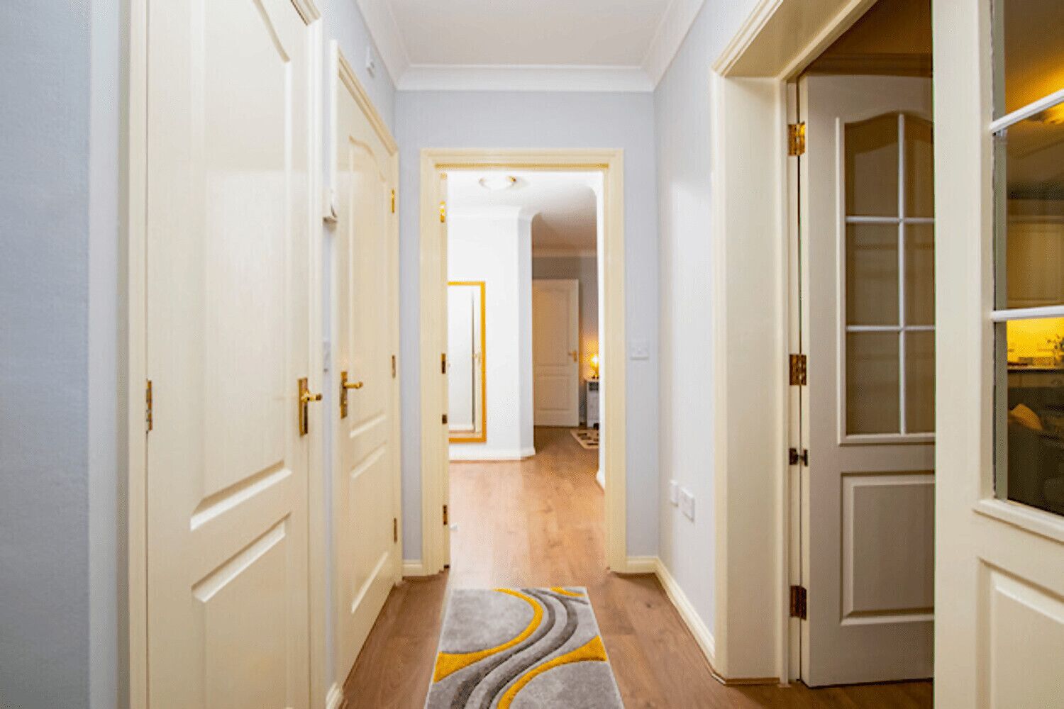 A hallway with white doors, a carpet with a geometric pattern, and a wooden floor.