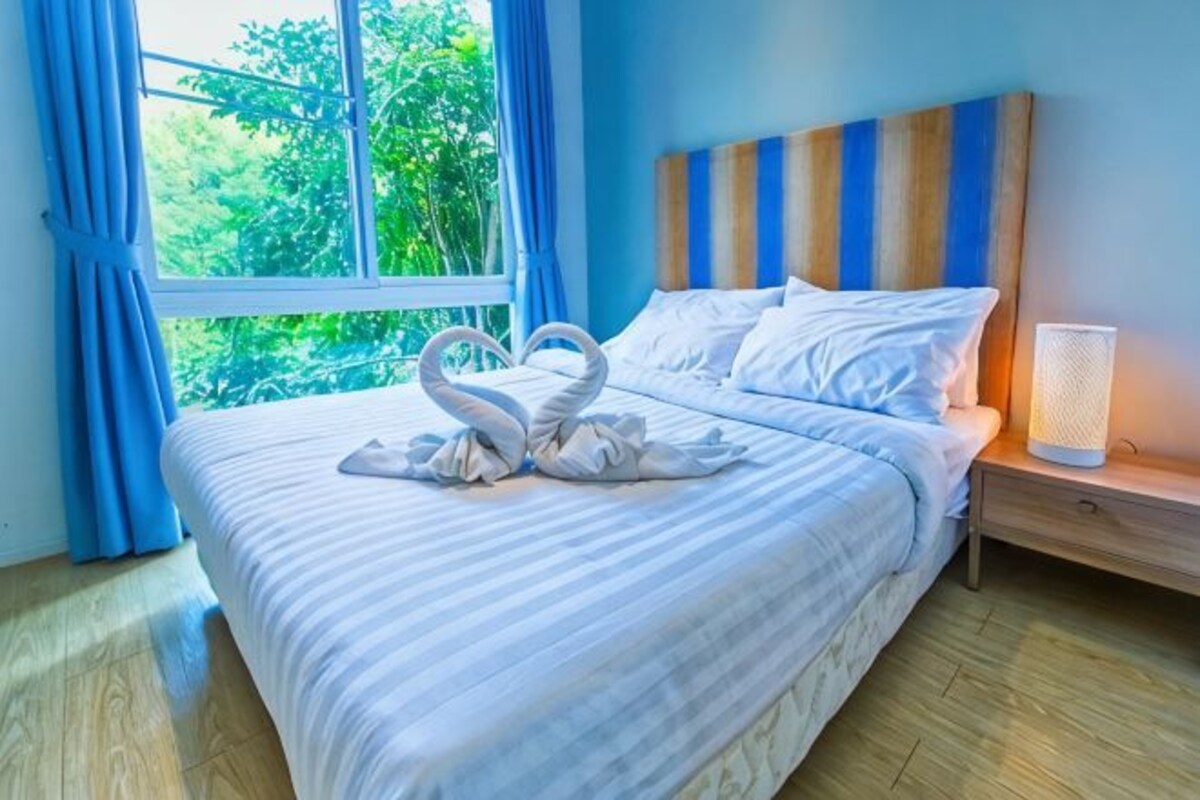 A hotel room with a bed, a nightstand, a lamp, and a window with curtains.